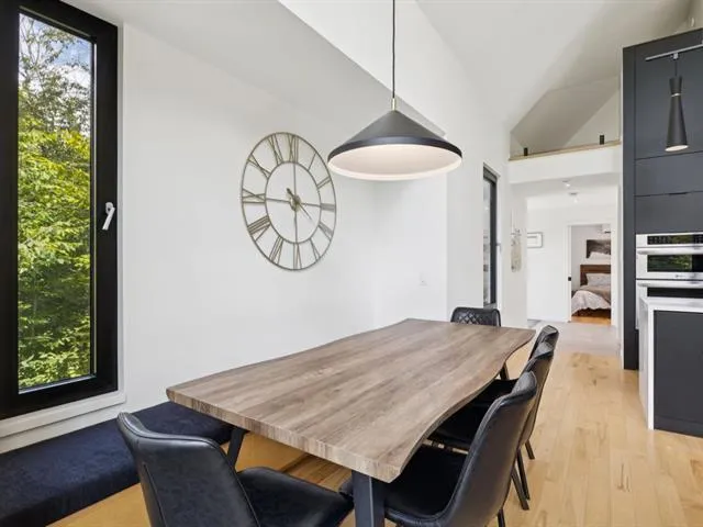 Open concept living with dining, kitchen island, fireplace and floor-to-ceiling forest views